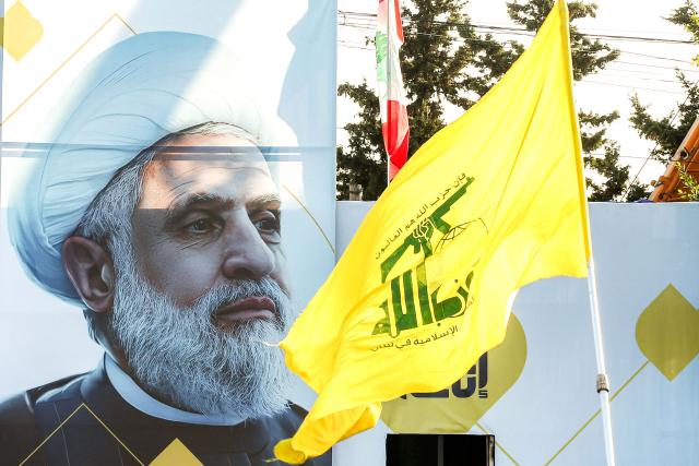 (FILES) A large picture of Naim Qassem, leader of the Lebanese Shiite movement Hezbollah, is displayed near the party's yellow flag, during a ceremony marking the first anniversary of Israel's assassination of the party's former leader and other group leaders, in the town of Deir Qanoun al-Nahr near the city of Tyre, in southern Lebanon on September 27, 2025. Hezbollah leader Naim Qassem rejected Lebanon's planned direct negotiations with Israel on April 27, 2026, calling them a "grave sin" that will destabilise Lebanon. Lebanon and Israel's US ambassadors held two meetings in Washington over the past weeks, the first of their kind in decades. (Photo by MAHMOUD ZAYYAT / AFP)
