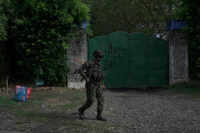 A Colombian soldier walks past a metal garage door bearing the inscription “FARC-EP”, the Spanish acronym for the Revolutionary Armed Forces of Colombia – People’s Army, in Jamundi, Valle del Cauca department, Colombia, on April 27, 2026. At least 31 guerrilla attacks were recorded in southwestern Colombia over the weekend, including the detonation of a bomb on a highway that killed 21 people, according to the latest government toll. (Photo by Joaquin SARMIENTO / AFP)
