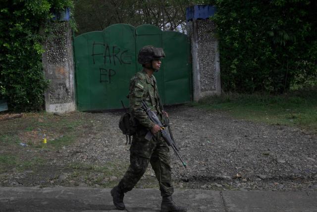 A Colombian soldier walks past a metal garage door bearing the inscription “FARC-EP”, the Spanish acronym for the Revolutionary Armed Forces of Colombia – People’s Army, in Jamundi, Valle del Cauca department, Colombia, on April 27, 2026. At least 31 guerrilla attacks were recorded in southwestern Colombia over the weekend, including the detonation of a bomb on a highway that killed 21 people, according to the latest government toll. (Photo by Joaquin SARMIENTO / AFP)