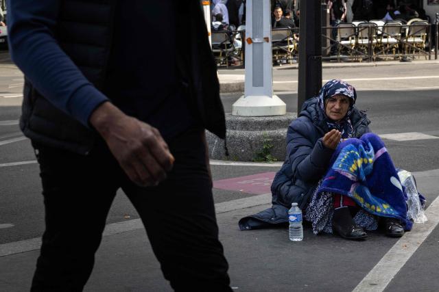 A pedestrian wals past a homeless person on a sidewalk in Paris on April 25, 2026. (Photo by JOEL SAGET / AFP)