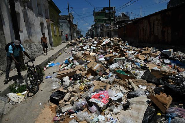Locals walk past garbage piled up on a street in Havana on April 27, 2026. (Photo by Yamil LAGE / AFP)