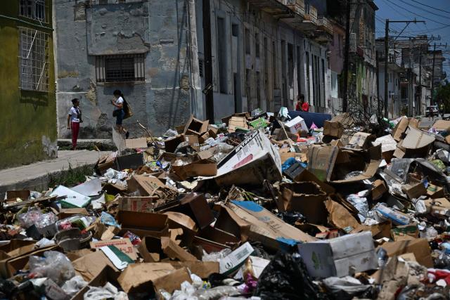 Locals walk past garbage piled up on a street in Havana on April 27, 2026. (Photo by Yamil LAGE / AFP)