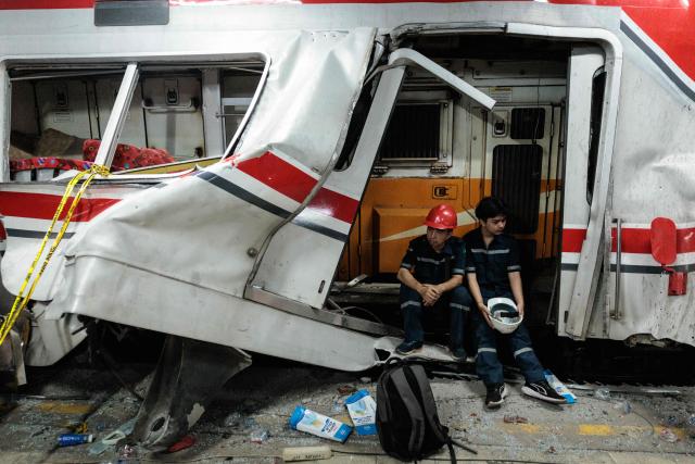 Workers sit at the site of a train collision as rescuers work to save five survivors trapped inside a carriage after a passenger train locomotive pierced through the rear car of a commuter train at Bekasi Timur station in Bekasi, West Java on April 28, 2026 (Photo by Yasuyoshi Chiba / AFP)