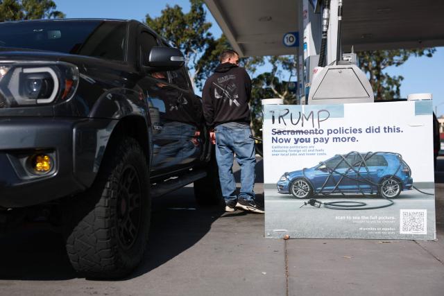 A vandalized sign about politicians, foreign oil, and gasoline taxes shows "Sacramento" crossed out and replaced with "Trump" reading, "Trump Policies Did This. Now You Pay More" is seen as a driver fuels a pickup truck at a Chevron gas station in El Segundo, California, on April 27, 2026. The US Treasury Department said on April 14 that it does not plan to renew a temporary easing of sanctions on Iranian oil that aimed to ease war-related supply shocks. (Photo by Patrick T. Fallon / AFP)