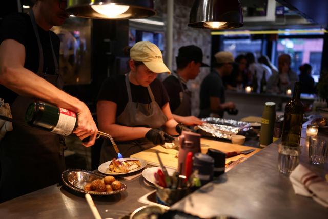 A cook prepares rotisserie chicken with potatoes during dinner service at the French restaurant Gigi’s in the Brooklyn borough of New York on April 26, 2026. Hugo Hivernat's restaurant was only open for a few days before he got dragged into New York City's cost of living row over a portion of half chicken priced at $40. For some on social media, the cost highlights how dining has become prohibitively expensive in the most populous US city. But Hivernat insists his business is barely making a profit. (Photo by CHARLY TRIBALLEAU / AFP)