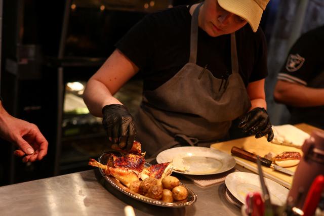 A cook prepares rotisserie chicken with potatoes during dinner service at the French restaurant Gigi’s in the Brooklyn borough of New York on April 26, 2026. Hugo Hivernat's restaurant was only open for a few days before he got dragged into New York City's cost of living row over a portion of half chicken priced at $40. For some on social media, the cost highlights how dining has become prohibitively expensive in the most populous US city. But Hivernat insists his business is barely making a profit. (Photo by CHARLY TRIBALLEAU / AFP)