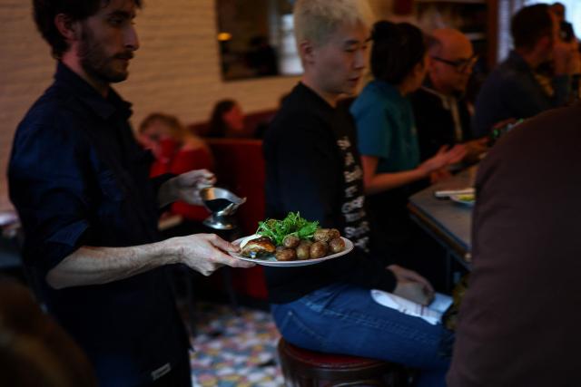 A waiter serves rotisserie chicken with potatoes during dinner service at the French restaurant Gigi’s in the Brooklyn borough of New York on April 26, 2026. Hugo Hivernat's restaurant was only open for a few days before he got dragged into New York City's cost of living row over a portion of half chicken priced at $40. For some on social media, the cost highlights how dining has become prohibitively expensive in the most populous US city. But Hivernat insists his business is barely making a profit. (Photo by CHARLY TRIBALLEAU / AFP)