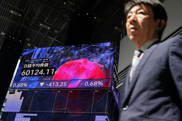 A man walks under an electronic quotation board displaying the Nikkei Stock Average on the Tokyo Stock Exchange along a street in Tokyo on April 28, 2026. (Photo by Kazuhiro NOGI / AFP)