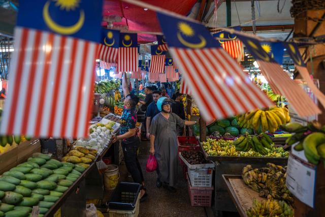 People browse for produce under Malaysian national flags at a fruit market in Kuala Lumpur on April 28, 2026. (Photo by Mohd Rasfan / AFP)