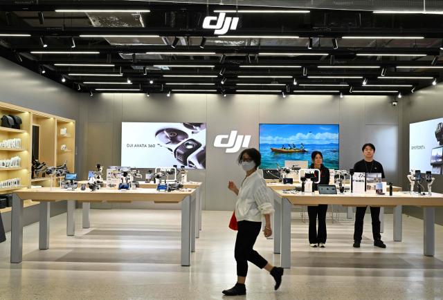 A woman walks past a DJI (Da-Jiang Innovators) store at a mall in Beijing on April 28, 2026. On May 1, 2026 Beijing government will ban new consumer drone sales. (Photo by Adek BERRY / AFP)