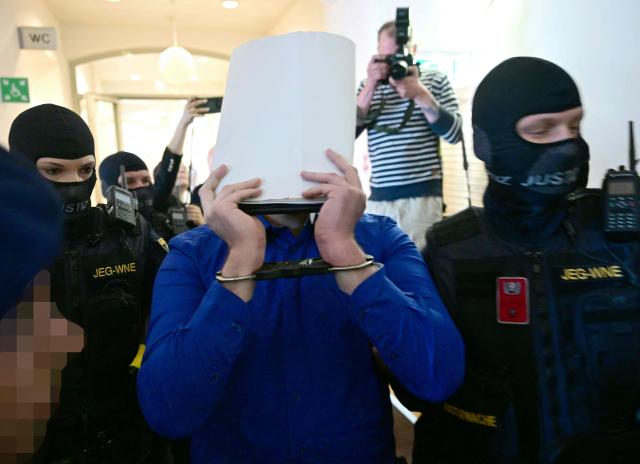 A defendant in handcuffs is escorted to the courtroom by justice officers as a trial starts at court in Wiener Neustadt, Austria, on April 28, 2026, over a plot to attack a Taylor Swift concert in Vienna. The main suspect, who has been in detention since his arrest in August 2024, is facing terror offenses and other charges, prosecutors said. (Photo by ROLAND SCHLAGER / APA / AFP) / Austria OUT