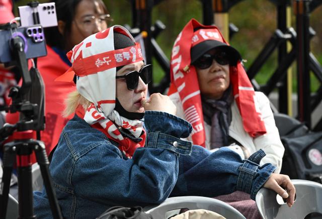 Supporters of South Korea's former president Yoon Suk Yeol and his wife Kim Keon Hee react as they watch a live stream of the trial of the former first lady on a street near the Seoul High Court in Seoul on April 28, 2026. A South Korean appeals court increased the corruption sentence for former first lady Kim Keon Hee on April 28 to four years in jail, up from 20 months, after finding her guilty of stock manipulation and bribery. (Photo by Jung Yeon-je / AFP)