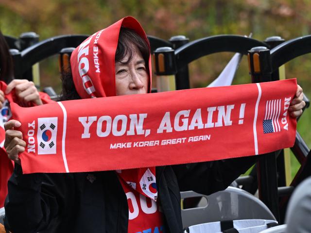 A supporter of South Korea's former president Yoon Suk Yeol and his wife Kim Keon Hee holds a banner reading "Yoon, Again!" as she watches a live stream of the trial of the former first lady on a street near the Seoul High Court in Seoul on April 28, 2026. A South Korean appeals court increased the corruption sentence for former first lady Kim Keon Hee on April 28 to four years in jail, up from 20 months, after finding her guilty of stock manipulation and bribery. (Photo by Jung Yeon-je / AFP)