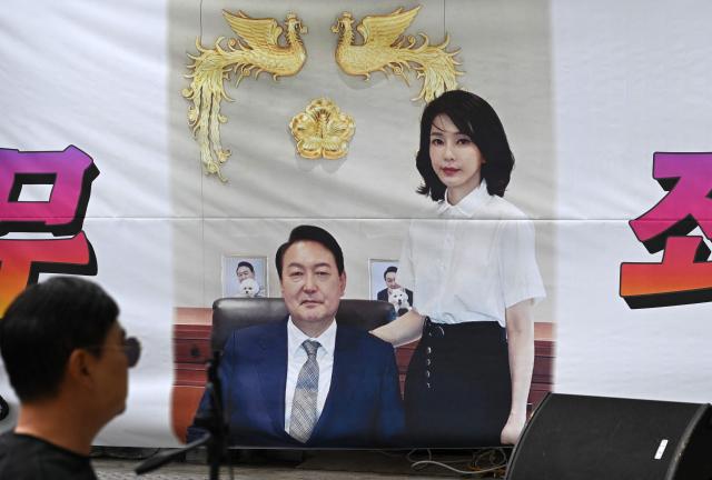 A man walks past a banner showing a picture of South Korea's former president Yoon Suk Yeol and his wife Kim Keon Hee on a street near the Seoul High Court in Seoul on April 28, 2026. A South Korean appeals court increased the corruption sentence for former first lady Kim Keon Hee on April 28 to four years in jail, up from 20 months, after finding her guilty of stock manipulation and bribery. (Photo by Jung Yeon-je / AFP)