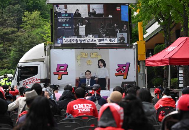 Supporters of South Korea's former president Yoon Suk Yeol and his wife Kim Keon Hee watch a live stream of the trial of the former first lady on a street near the Seoul High Court in Seoul on April 28, 2026. A South Korean appeals court increased the corruption sentence for former first lady Kim Keon Hee on April 28 to four years in jail, up from 20 months, after finding her guilty of stock manipulation and bribery. (Photo by Jung Yeon-je / AFP)