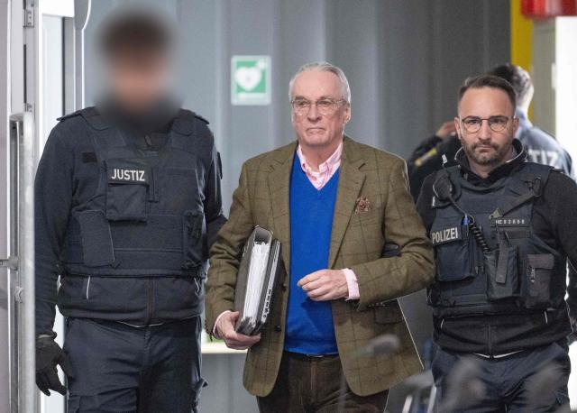 Defendant Prince Heinrich XIII Reuss (C) arrives at the courtroom for the continuation of the so-called "Reichsbuerger" trial against himself, a former MP and ex-army officers accused of masterminding a conspiracy theory-driven plot to attack the German parliament and topple the government, on April 28, 2026 in Frankfurt am Main, western Germany. In one of the biggest cases heard by German courts in decades, prosecutors accuse the group of preparing a "treasonous undertaking" to storm the Bundestag (German parliament) and take MPs hostage. The proceedings at the regional court in Frankfurt are the second of three trials against defendants linked to the putsch plan. Eight suspected members of the coup plot are taking the stand in Frankfurt, as well as one woman accused of supporting their efforts to overthrow then Chancellor Olaf Scholz's government. (Photo by Boris Roessler / POOL / AFP)