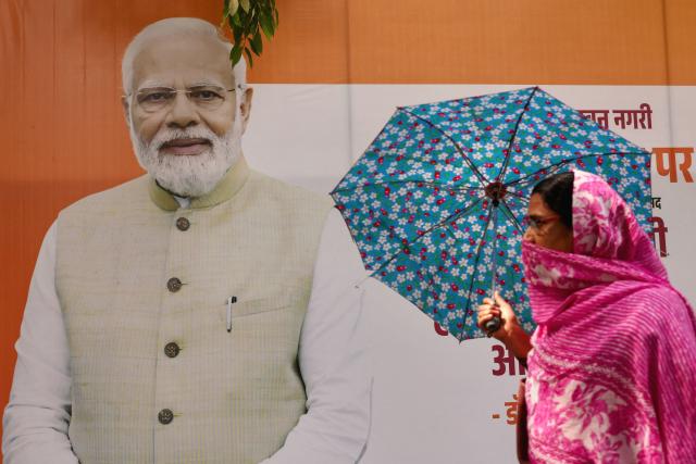 A woman carrying an umbrella walks past a hoarding of India's Prime Minister Narendra Modi as she arrives to attend a public meeting for women addressed by him in Varanasi on April 28, 2026. (Photo by Niharika KULKARNI / AFP)