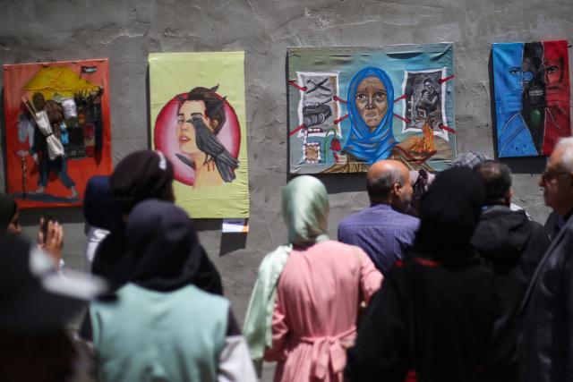 Displaced Palestinian people look at paintings at an open-air art exhibition at the Bureij camp for Palestinian refugees in the central Gaza Strip on April 28, 2026. The majority of Gaza's 2.4 million people have been displaced, often multiple times, by the war that began with Hamas's attack on southern Israel on October 7, 2023. With displaced families living in tented camps, with serious concerns raised about their living conditions. (Photo by Eyad Baba / AFP)