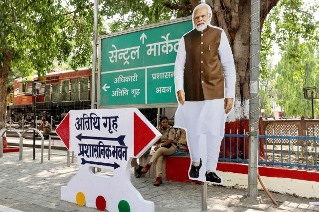 A police personnel sits next to a cut-out of India's Prime Minister Narendra Modi before his arrival for a public meeting for women in Varanasi on April 28, 2026. (Photo by Niharika KULKARNI / AFP)