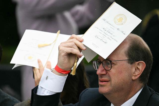 An attendee protects himself from the rain while waiting for US President Donald Trump and First Lady Melania Trump to greet Britain's King Charles III and Queen Camilla for an arrival ceremony on the South Lawn of the White House in Washington, DC, on April 28, 2026. (Photo by Jim WATSON / AFP)