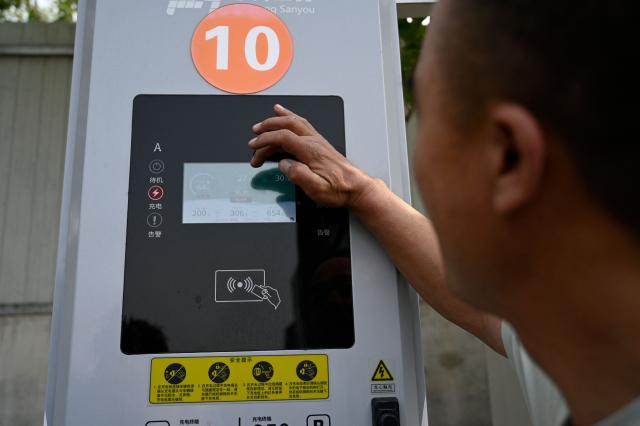 This picture taken on April 23, 2026 shows a driver checking the status of his electric truck at a charging station in Beijing. At a dusty lot an hour outside Beijing, a steady stream of vehicles come and go for a quick battery charge -- just one node in China's rapidly expanding network of electric trucks. (Photo by WANG Zhao / AFP) / To go with AFP story China-tech-logistics-auto-show, FOCUS by Peter CATTERALL