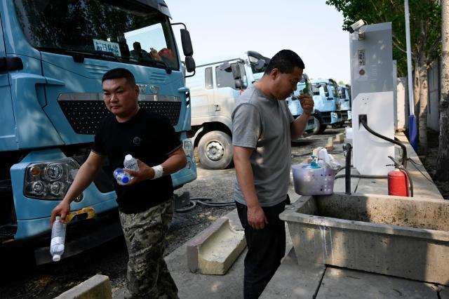This picture taken on April 23, 2026 shows a driver brushing his teeth while charging his electric truck at a station in Beijing. At a dusty lot an hour outside Beijing, a steady stream of vehicles come and go for a quick battery charge -- just one node in China's rapidly expanding network of electric trucks. (Photo by WANG Zhao / AFP) / To go with AFP story China-tech-logistics-auto-show, FOCUS by Peter CATTERALL