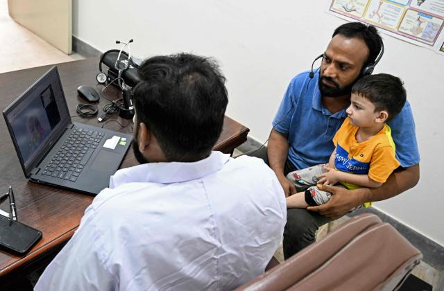 This photograph taken on April 7, 2026 shows Muhammad Adil (C), receiving an online and free doctor consultation for his son at a clinic of digital health firm Sehat Kahani in Karachi. Gallup surveys and doctors' associations suggest more than a third of Pakistani female medical graduates never enter the profession -- or leave it after marriage -- due to lack of family support, poor childcare facilities, and harassment. But an initiative by digital health firm Sehat Kahani helped women back into the workforce by providing a digital platform to connect home-based, mostly female doctors, with patients in underserved communities. (Photo by Rizwan TABASSUM / AFP)