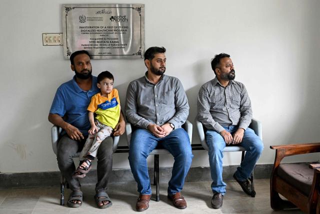 This photograph taken on April 7, 2026 shows Muhammad Adil (L), waiting for an online and free doctor consultation for his son at a clinic of digital health firm Sehat Kahani in Karachi. Gallup surveys and doctors' associations suggest more than a third of Pakistani female medical graduates never enter the profession -- or leave it after marriage -- due to lack of family support, poor childcare facilities, and harassment. But an initiative by digital health firm Sehat Kahani helped women back into the workforce by providing a digital platform to connect home-based, mostly female doctors, with patients in underserved communities. (Photo by Rizwan TABASSUM / AFP)