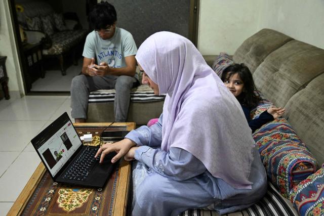 This photograph taken on April 7, 2026 shows Saniya Jafri, a doctor and telemedicine practitioner with the digital health firm Sehat Kahani, conducting online patient consultations as she sits next to her children at their residence in Karachi. Gallup surveys and doctors' associations suggest more than a third of Pakistani female medical graduates never enter the profession -- or leave it after marriage -- due to lack of family support, poor childcare facilities, and harassment. But an initiative by digital health firm Sehat Kahani helped women back into the workforce by providing a digital platform to connect home-based, mostly female doctors, with patients in underserved communities. (Photo by Rizwan TABASSUM / AFP)