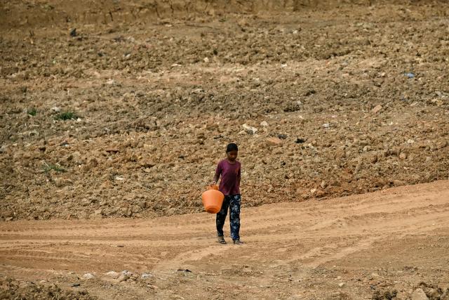 A girl carries an empty water container across the parched bed of Ulsoor Lake during an ongoing large-scale desilting and restoration project in Bengaluru on April 29, 2026. (Photo by Idrees MOHAMMED / AFP)