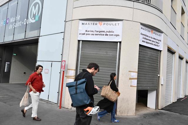 Pedestrians walk past a Master Poulet, a fast food restaurant  specialised in low-cost halal grilled chicken, in Saint-Ouen, a northern suburb of Paris on April 29, 2026. In Saint-Ouen (Seine-Saint-Denis), a showdown is pitting the halal fast-food chain Master Poulet against the Socialist mayor Karim Bouamrane, amid mutual accusations of gentrifying the city and promoting "junk food". (Photo by Martin LELIEVRE / AFP)