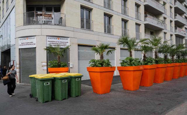 Pedestrians walk past a Master Poulet, a fast food restaurant specialised in halal grilled chicken, after the mayor had several gigantic orange flower pots installed all around the restaurant to block its access in Saint-Ouen, a northern suburb of Paris on April 29, 2026. In Saint-Ouen (Seine-Saint-Denis), a showdown is pitting the halal fast-food chain Master Poulet against the Socialist mayor Karim Bouamrane, amid mutual accusations of gentrifying the city and promoting "junk food". (Photo by Martin LELIEVRE / AFP)