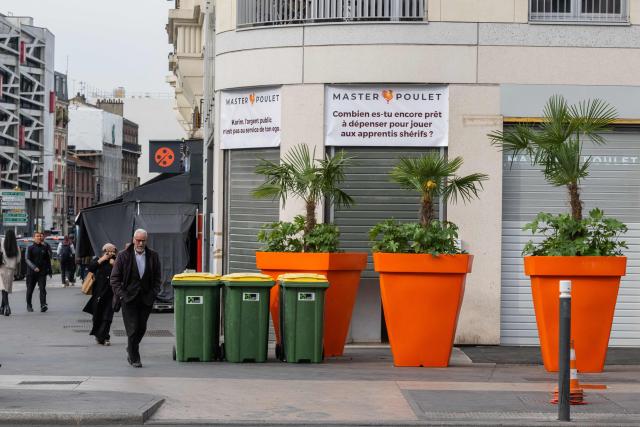 Pedestrians walk past a Master Poulet, a fast food restaurant specialised in halal grilled chicken, after the mayor had several gigantic orange flower pots installed all around the restaurant to block its access in Saint-Ouen, a northern suburb of Paris on April 29, 2026. In Saint-Ouen (Seine-Saint-Denis), a showdown is pitting the halal fast-food chain Master Poulet against the Socialist mayor Karim Bouamrane, amid mutual accusations of gentrifying the city and promoting "junk food". (Photo by Martin LELIEVRE / AFP)