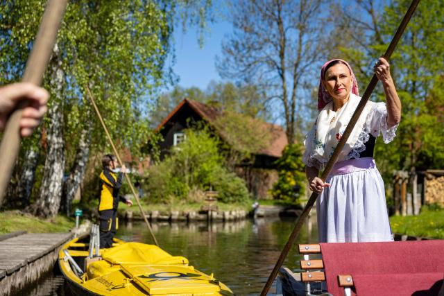 A woman wearing a traditional Sorb outfit (R) manouvers a so-called "Spreewaldkahn" barge carrying tourists along a canal in the Spreewald region in Luebbenau, eastern Germany, as in background can be seen a boat of the postal service, on April 29, 2026. (Photo by Odd ANDERSEN / AFP)