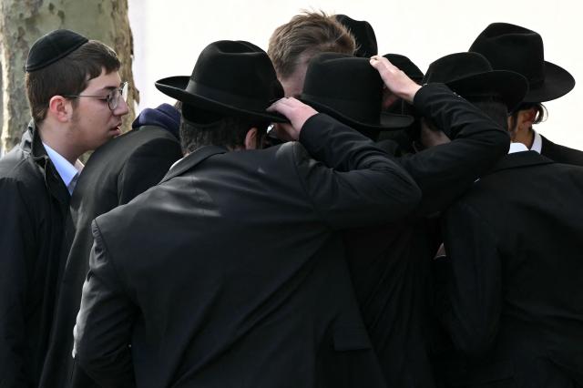 People gather to watch footage on a smartphone, near to a Police cordon in the Golders Green neighbourhood of north London, on April 29, 2026, after two people were stabbed, and a suspect arrested. Two people were stabbed Wednesday in north London, Jewish groups said, following a series of arson attacks targeting Jewish sites in the area, as UK Prime Minister Keir Starmer called the incident "deeply concerning". A man was arrested after he was seen running with a knife "attempting to stab Jewish members of the public", the Shomrim Jewish neighbourhood watch said on social media. (Photo by JUSTIN TALLIS / AFP)