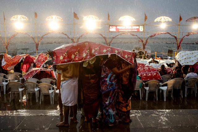 Tourists take shelter under sheets during rainfall as they wait to attend evening prayers at Dashashwamedh ghat along the banks of river Ganges in Varanasi on April 29, 2026. (Photo by Niharika KULKARNI / AFP)
