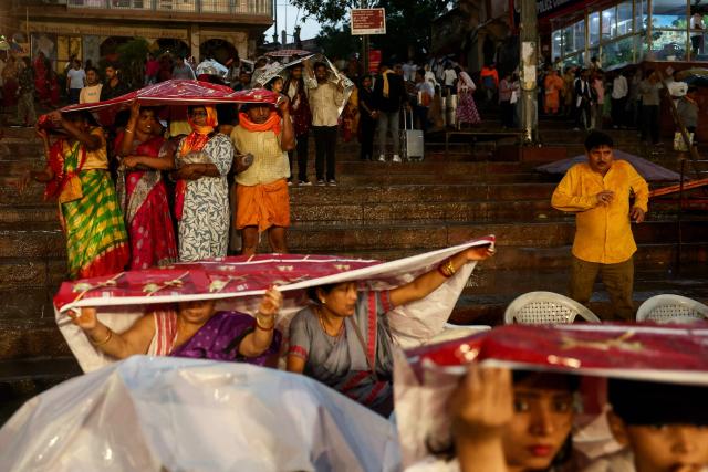 Tourists take shelter under sheets during rainfall as they wait to attend evening prayers at Dashashwamedh ghat along the banks of river Ganges in Varanasi on April 29, 2026. (Photo by Niharika KULKARNI / AFP)