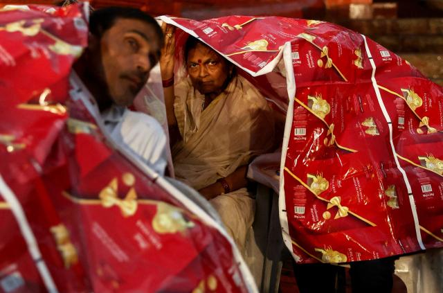 A tourist looks on as she takes shelter under a sheet during rainfall while waiting to attend evening prayers at Dashashwamedh ghat along the banks of river Ganges in Varanasi on April 29, 2026. (Photo by Niharika KULKARNI / AFP)