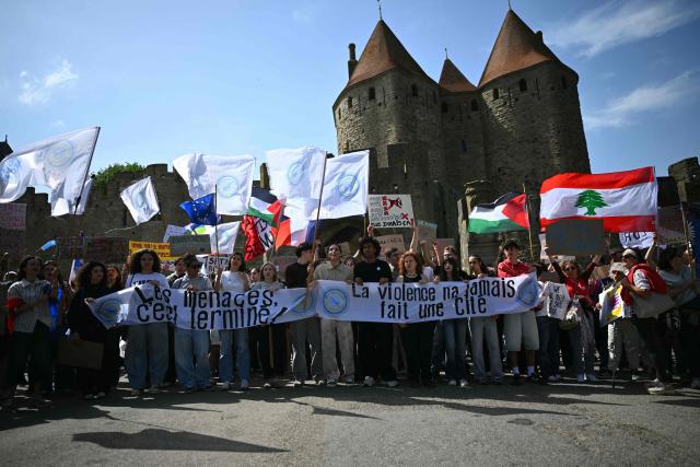 Protesters hold Lebanese, Palestinian and European flags and a banner reading "The threats are over. Violence has never built a city" as they demonstrate in front of the medieval citadel at the call of "Nous Carcassonne" collective against the decisions taken by Carcassonne's 'Rassemblement National' newly elected mayor, in Carcassonne, southwestern France on April 29, 2026. (Photo by LIONEL BONAVENTURE / AFP)