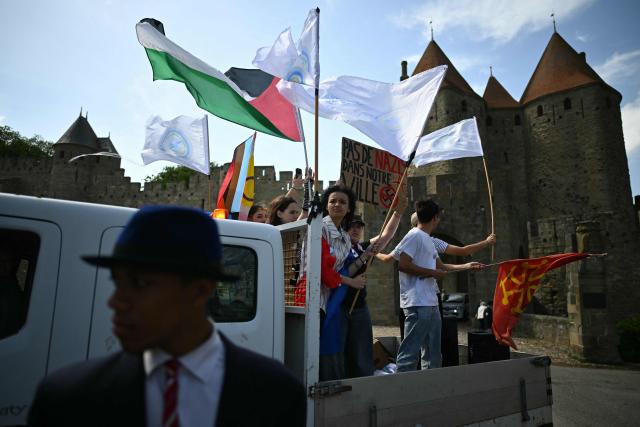 Protesters hold Palestinian and Occitanie flags and a placard reading "No nazis in our city" as they demonstrate in front of the medieval citadel at the call of "Nous Carcassonne" collective against the decisions taken by Carcassonne's 'Rassemblement National' newly elected mayor, in Carcassonne, southwestern France on April 29, 2026. (Photo by LIONEL BONAVENTURE / AFP)