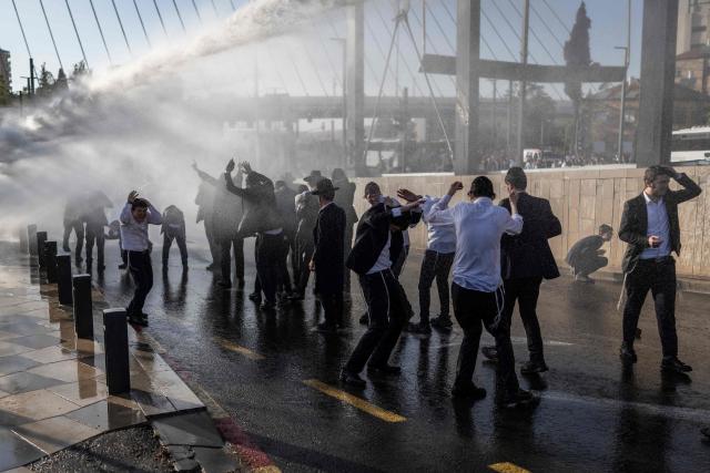 Israeli ultra-Orthodox Jews take cover from a water cannon spray during a protest against conscription by blocking the entrance to Jerusalem, on April 29, 2026. They oppose a change to the law on compulsory military service, from which the ultra-Orthodox community has traditionally been exempt. Under a provision established when the country was founded in 1948 – when the ultra-Orthodox community was small – men who dedicate themselves full-time to the study of Jewish sacred texts are effectively exempt. (Photo by ilia YEFIMOVICH / AFP) / 