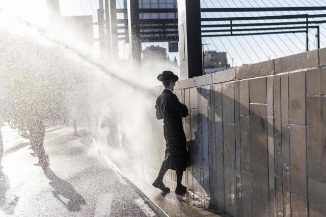 An Israeli ultra-Orthodox Jew is sprayed by a water cannon during a protest against conscription by blocking the entrance to Jerusalem, on April 29, 2026. They oppose a change to the law on compulsory military service, from which the ultra-Orthodox community has traditionally been exempt. Under a provision established when the country was founded in 1948 – when the ultra-Orthodox community was small – men who dedicate themselves full-time to the study of Jewish sacred texts are effectively exempt. (Photo by ilia YEFIMOVICH / AFP) / 