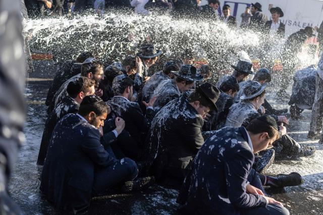 TOPSHOT - Israeli ultra-Orthodox Jews sit while being sprayed by a water cannon during a protest against conscription by blocking the entrance to Jerusalem, on April 29, 2026. They oppose a change to the law on compulsory military service, from which the ultra-Orthodox community has traditionally been exempt. Under a provision established when the country was founded in 1948 – when the ultra-Orthodox community was small – men who dedicate themselves full-time to the study of Jewish sacred texts are effectively exempt. (Photo by ilia YEFIMOVICH / AFP)