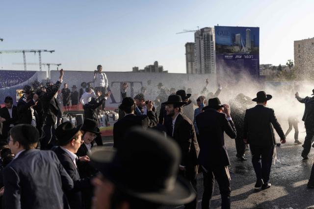 Israeli ultra-Orthodox Jews take cover from a water cannon spray during a protest against conscription by blocking the entrance to Jerusalem, on April 29, 2026. They oppose a change to the law on compulsory military service, from which the ultra-Orthodox community has traditionally been exempt. Under a provision established when the country was founded in 1948 – when the ultra-Orthodox community was small – men who dedicate themselves full-time to the study of Jewish sacred texts are effectively exempt. (Photo by ilia YEFIMOVICH / AFP) / 