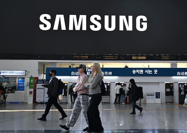 People walk past a large electronic screen showing the Samsung logo at a train station in Seoul on April 30, 2026. South Korean tech giant Samsung Electronics posted a record quarterly profit on April 30, driven by strong sales of chips crucial for artificial intelligence. (Photo by Jung Yeon-je / AFP)