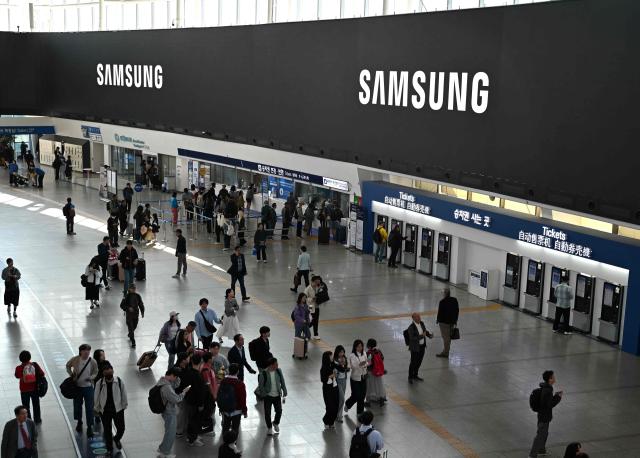 People walk past a large electronic screen showing the Samsung logo at a train station in Seoul on April 30, 2026. South Korean tech giant Samsung Electronics posted a record quarterly profit on April 30, driven by strong sales of chips crucial for artificial intelligence. (Photo by Jung Yeon-je / AFP)