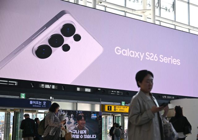 People walk past a large electronic screen advertising the Samsung Galaxy S26 smartphone at a train station in Seoul on April 30, 2026. South Korean tech giant Samsung Electronics posted a record quarterly profit on April 30, driven by strong sales of chips crucial for artificial intelligence. (Photo by Jung Yeon-je / AFP)