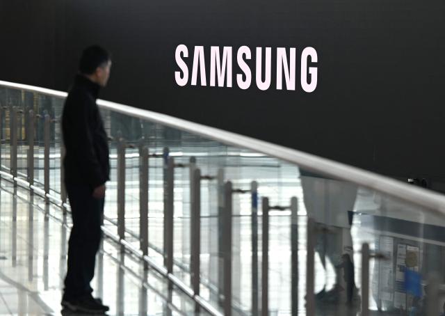 A man stands in front of a large electronic screen showing the Samsung logo at a train station in Seoul on April 30, 2026. South Korean tech giant Samsung Electronics posted a record quarterly profit on April 30, driven by strong sales of chips crucial for artificial intelligence. (Photo by Jung Yeon-je / AFP)