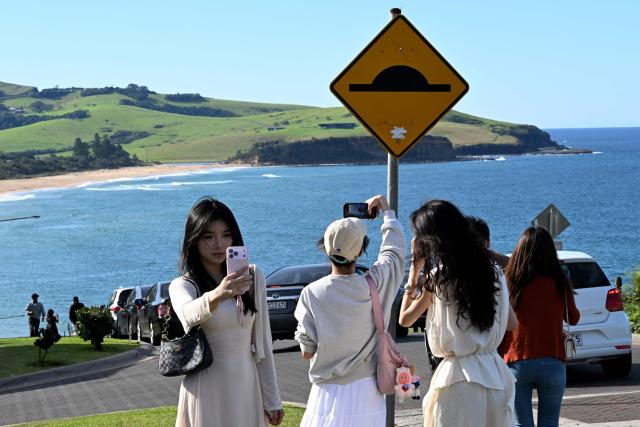This picture taken on April 27, 2026 shows tourists taking photos on a street in Gerringong, about a two-hour drive south of Sydney. Viral posts of an Australian street dubbed the country's "most beautiful" have enticed coachloads of visitors to a picturesque seaside town -- and locals have had enough of it. (Photo by Saeed KHAN / AFP) / To go with AFP story Australia-tourism-internet by Oliver Hotham