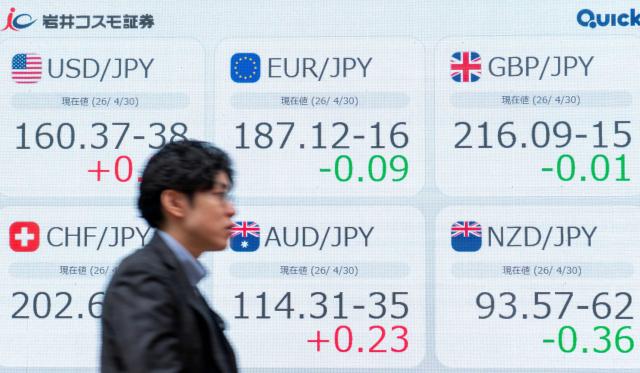 A man walks past an electronic quotation boards displaying the exchange rates between the Japanese yen and major world currencies including a rate against US dollar (top, L) along a street in Tokyo on April 30, 2026. (Photo by Kazuhiro NOGI / AFP)